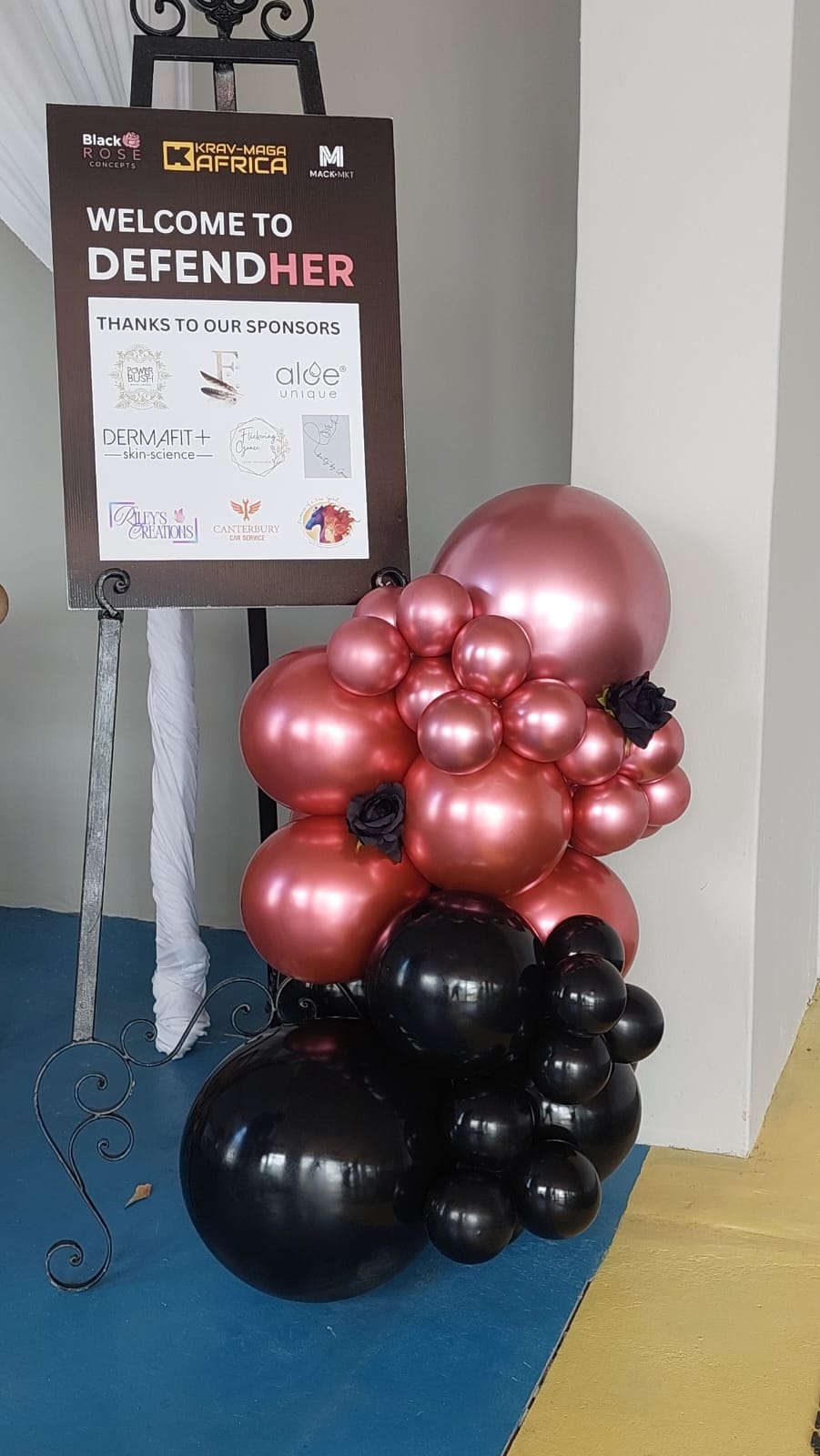 Welcome to DefendHer sign with rose-gold and black balloons