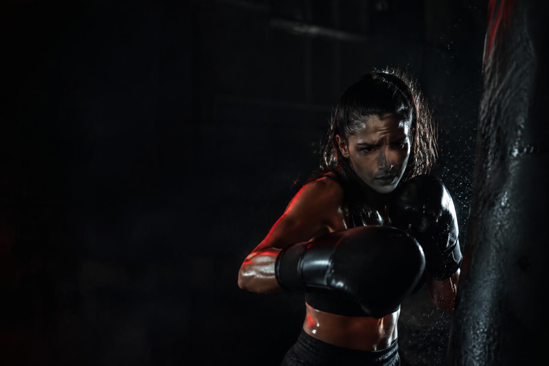 Woman boxer in black gloves striking a heavy bag